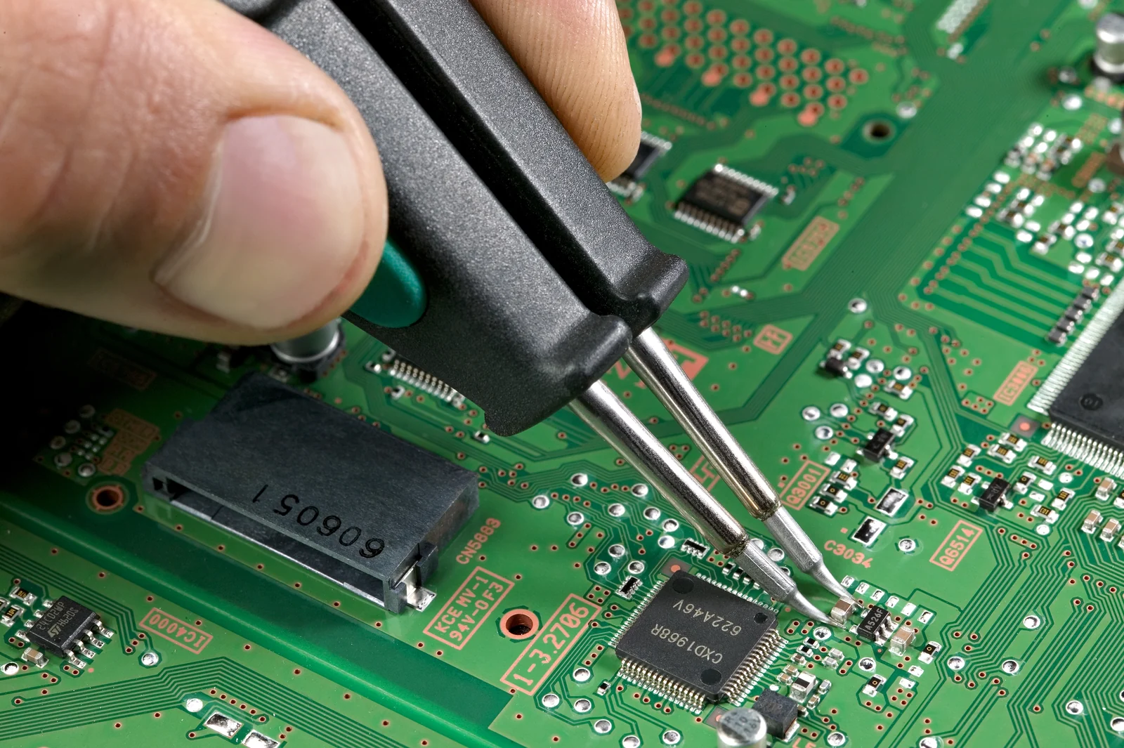 Soldering tweezers working on a small surface-mounted component on a circuit board.